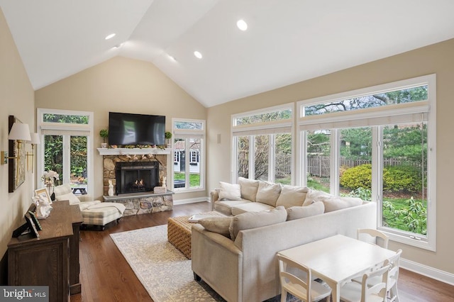 living area featuring high vaulted ceiling, a stone fireplace, recessed lighting, baseboards, and wood finished floors