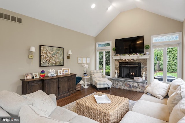 living room with high vaulted ceiling, plenty of natural light, a stone fireplace, and visible vents