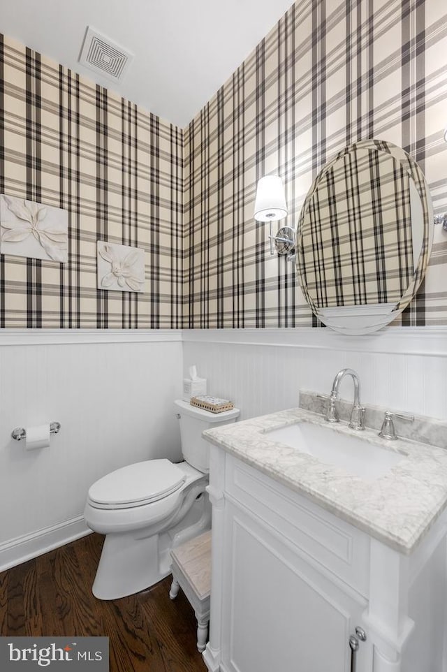 half bath with toilet, visible vents, wainscoting, and wood finished floors