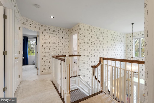 hall with light carpet, an upstairs landing, and wallpapered walls