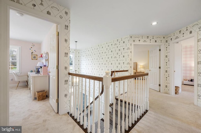 hallway featuring light colored carpet, wallpapered walls, an upstairs landing, and baseboards