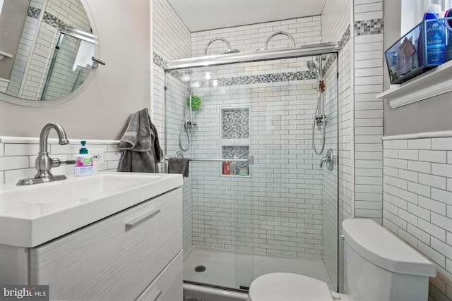 bathroom with tile walls, wainscoting, a stall shower, vanity, and toilet