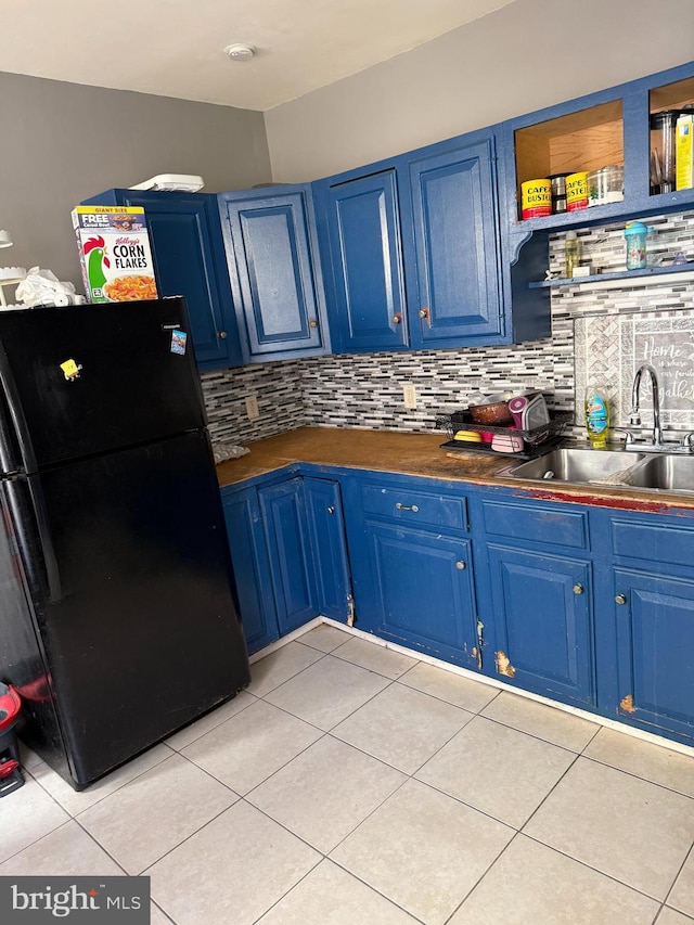 kitchen with a sink, light tile patterned floors, freestanding refrigerator, and blue cabinets