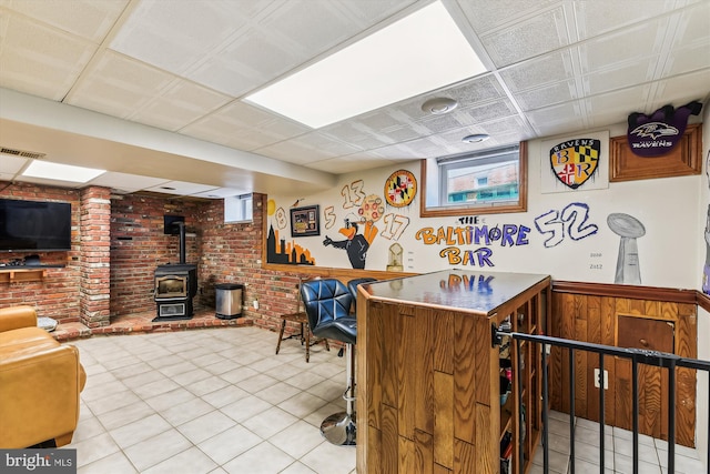 bar featuring visible vents, a wood stove, light tile patterned flooring, brick wall, and a wainscoted wall