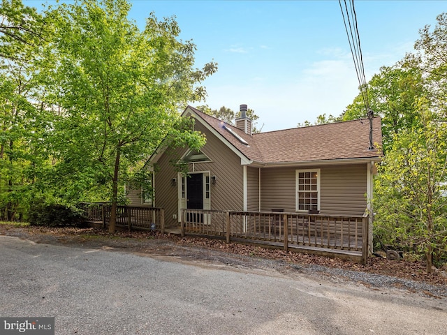 view of front of house with a shingled roof, a wooden deck, and a chimney