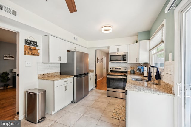 kitchen featuring appliances with stainless steel finishes, a sink, white cabinets, tasteful backsplash, and light stone countertops