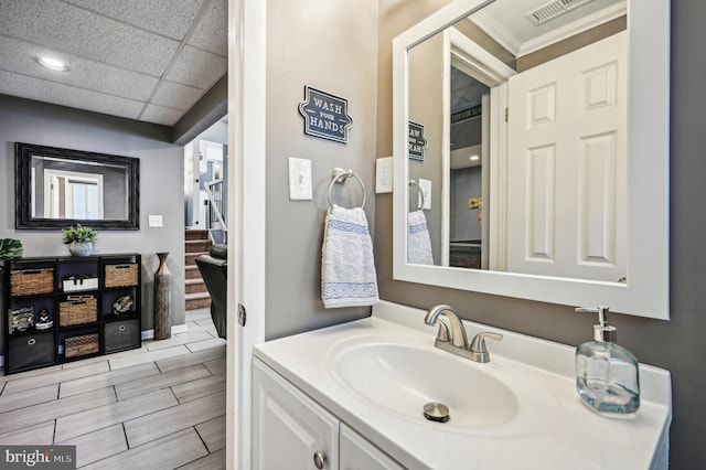 bathroom featuring vanity, a drop ceiling, ornamental molding, and wood finish floors