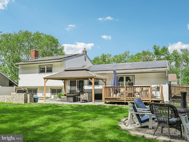 rear view of property featuring outdoor lounge area, a gazebo, a chimney, roof mounted solar panels, and a wooden deck