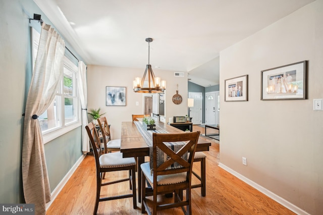dining space featuring baseboards, light wood-type flooring, a chandelier, and vaulted ceiling