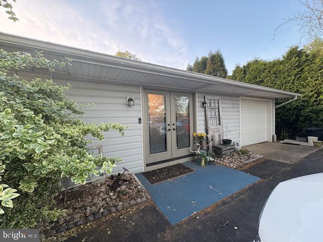 entrance to property featuring french doors, an attached garage, and concrete driveway