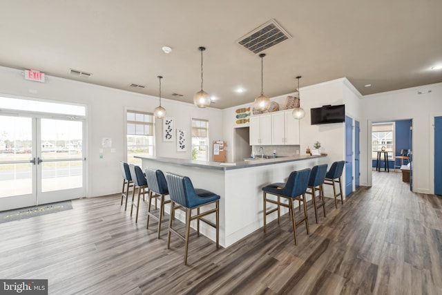 kitchen with a breakfast bar, a peninsula, wood finished floors, and visible vents