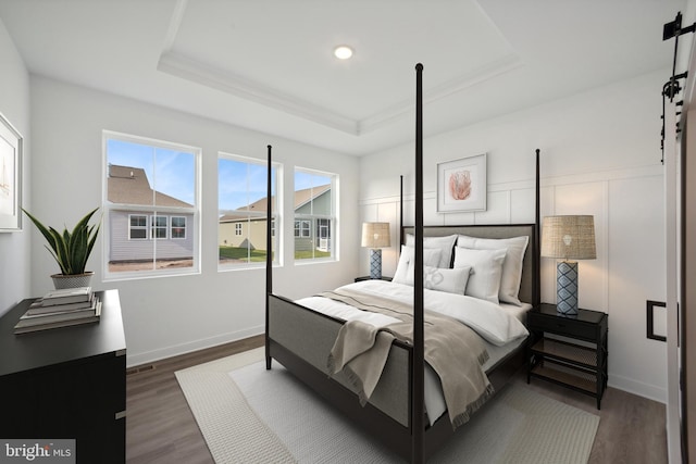 bedroom featuring baseboards, a barn door, a raised ceiling, and dark wood-style floors