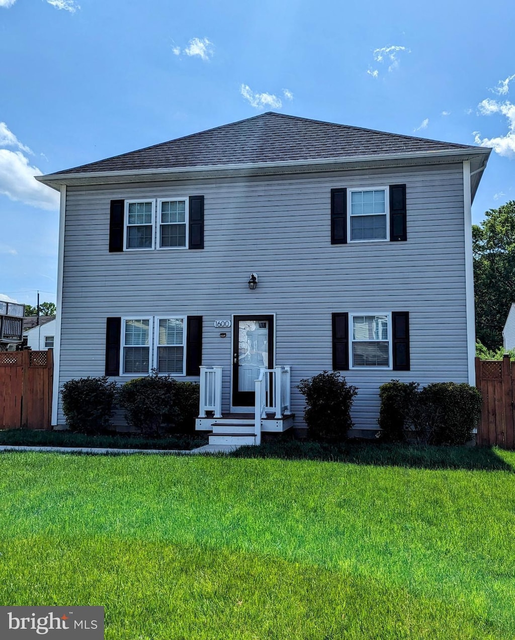 colonial home with a shingled roof, fence, and a front yard
