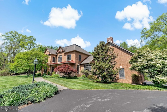 view of front of home featuring brick siding, a chimney, and a front yard