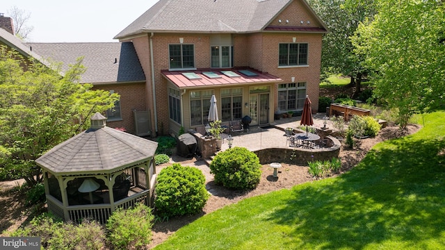rear view of property with a lawn, a standing seam roof, brick siding, a patio area, and a gazebo