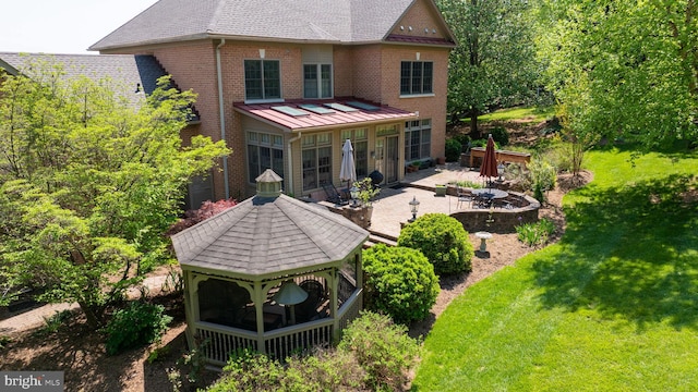 back of house featuring a gazebo, brick siding, a standing seam roof, a patio, and a yard