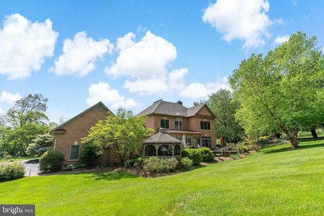rear view of property featuring a gazebo, a lawn, and brick siding