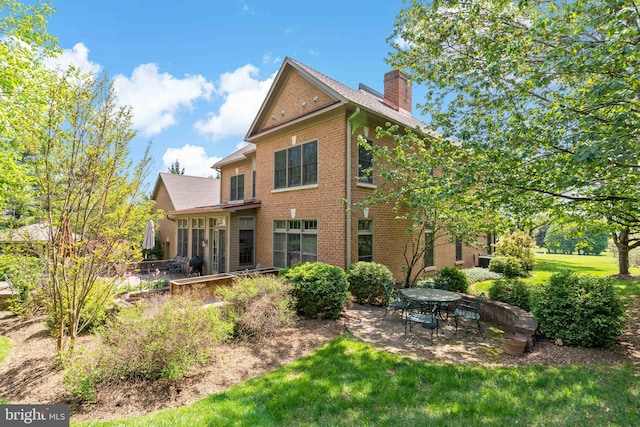 rear view of property featuring brick siding, a patio, a chimney, and a lawn