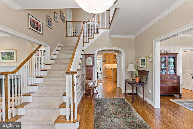 entryway featuring arched walkways, wood finished floors, baseboards, ornamental molding, and stairs