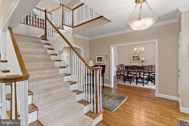 staircase with baseboards, ornamental molding, wood finished floors, and a notable chandelier