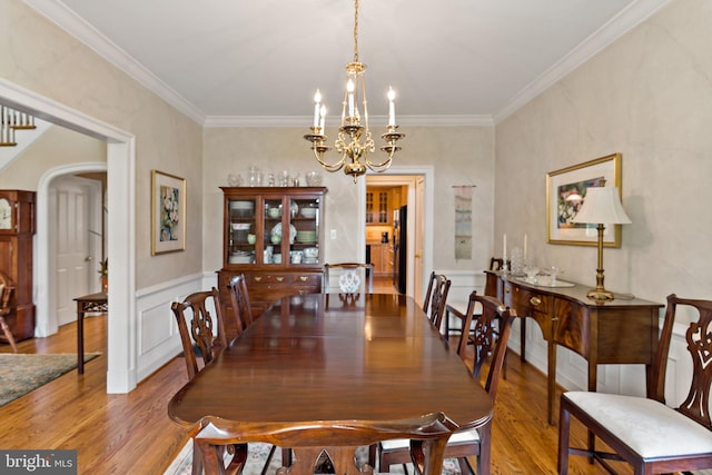 dining space with crown molding, arched walkways, wood finished floors, and a notable chandelier