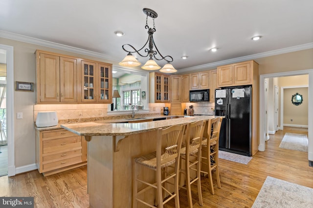 kitchen featuring light brown cabinetry, crown molding, a sink, a breakfast bar area, and black appliances