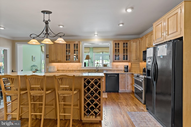 kitchen with crown molding, light wood-style floors, a kitchen bar, a sink, and black appliances