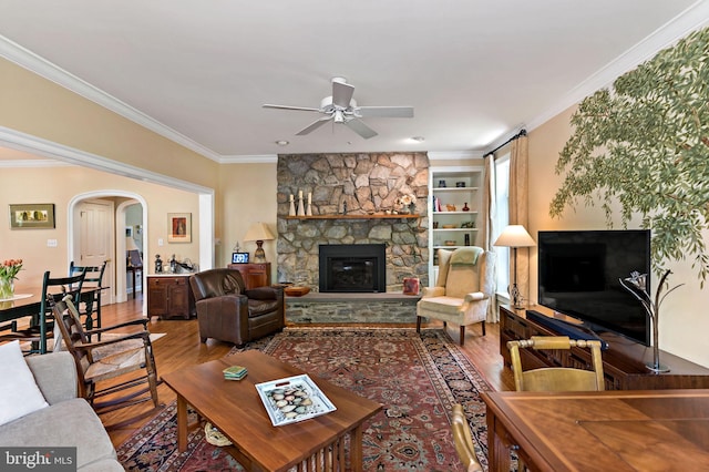 living area featuring a ceiling fan, arched walkways, a fireplace, wood finished floors, and ornamental molding