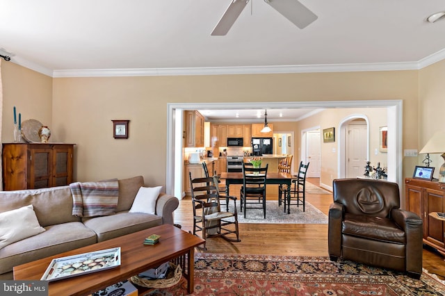 living room featuring arched walkways, ceiling fan, ornamental molding, and wood finished floors