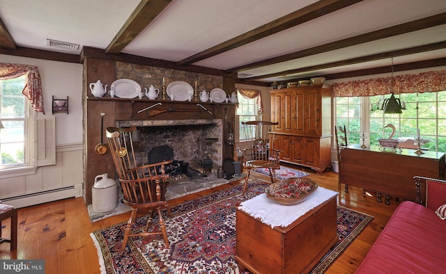 living area featuring baseboard heating, wainscoting, wood finished floors, beamed ceiling, and a large fireplace