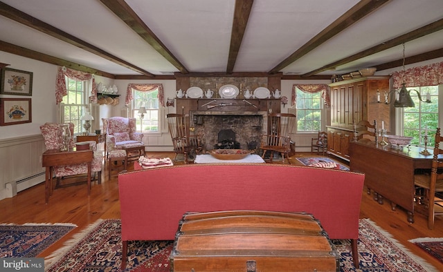 living area with wood finished floors, beamed ceiling, a fireplace, baseboard heating, and healthy amount of natural light