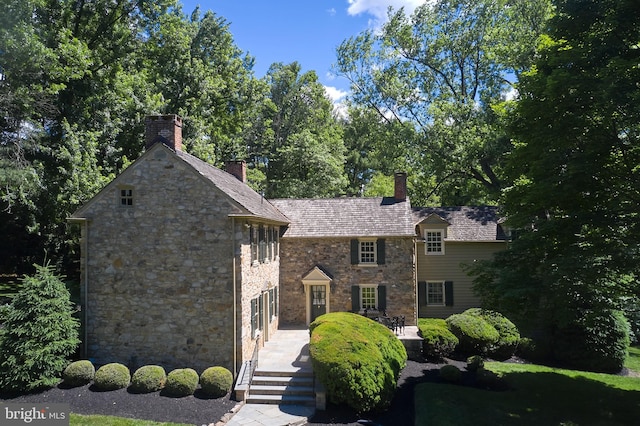 view of front of house with stone siding and a chimney