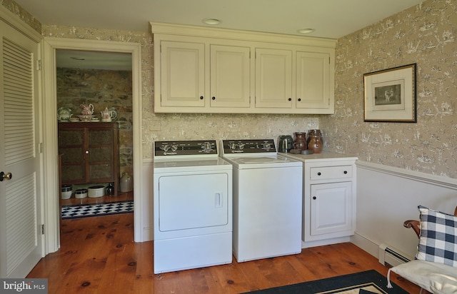laundry room featuring a wainscoted wall, cabinet space, wood finished floors, washing machine and dryer, and wallpapered walls