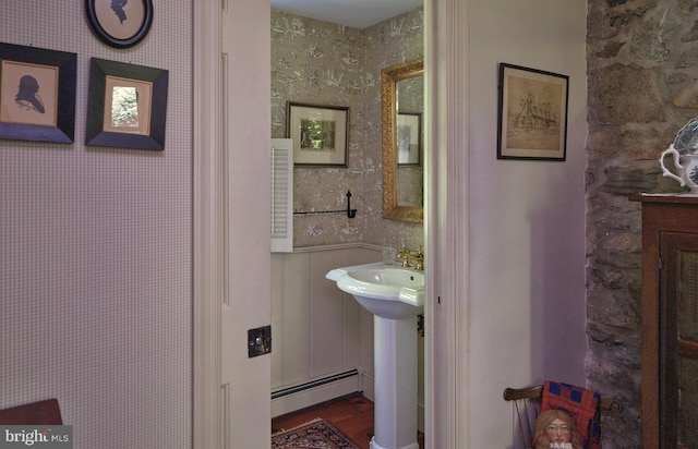 bathroom with a baseboard heating unit, wallpapered walls, wainscoting, and wood finished floors