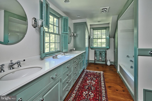 full bath featuring wood finished floors, double vanity, and a baseboard heating unit