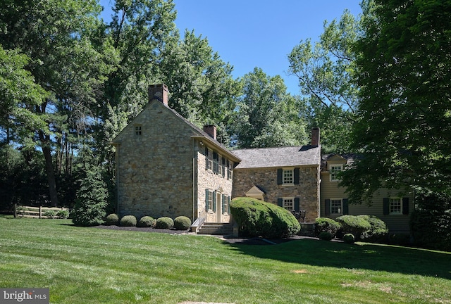 view of front of house featuring stone siding, a front yard, and a chimney