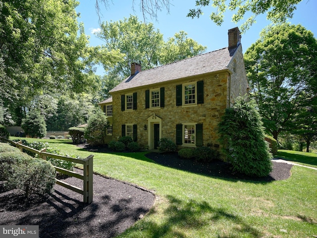 colonial house featuring stone siding, a chimney, and a front yard
