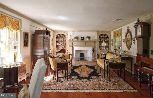 living area with built in shelves, wood-type flooring, crown molding, and a fireplace