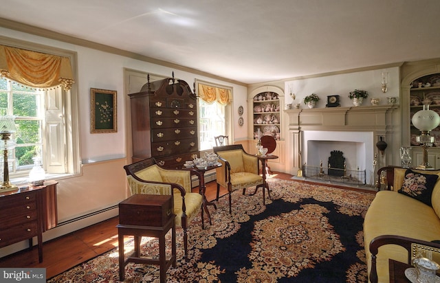 sitting room featuring a fireplace, healthy amount of natural light, crown molding, built in features, and wood finished floors