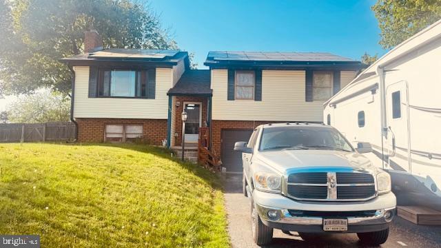bi-level home with a chimney, a front yard, a garage, brick siding, and fence