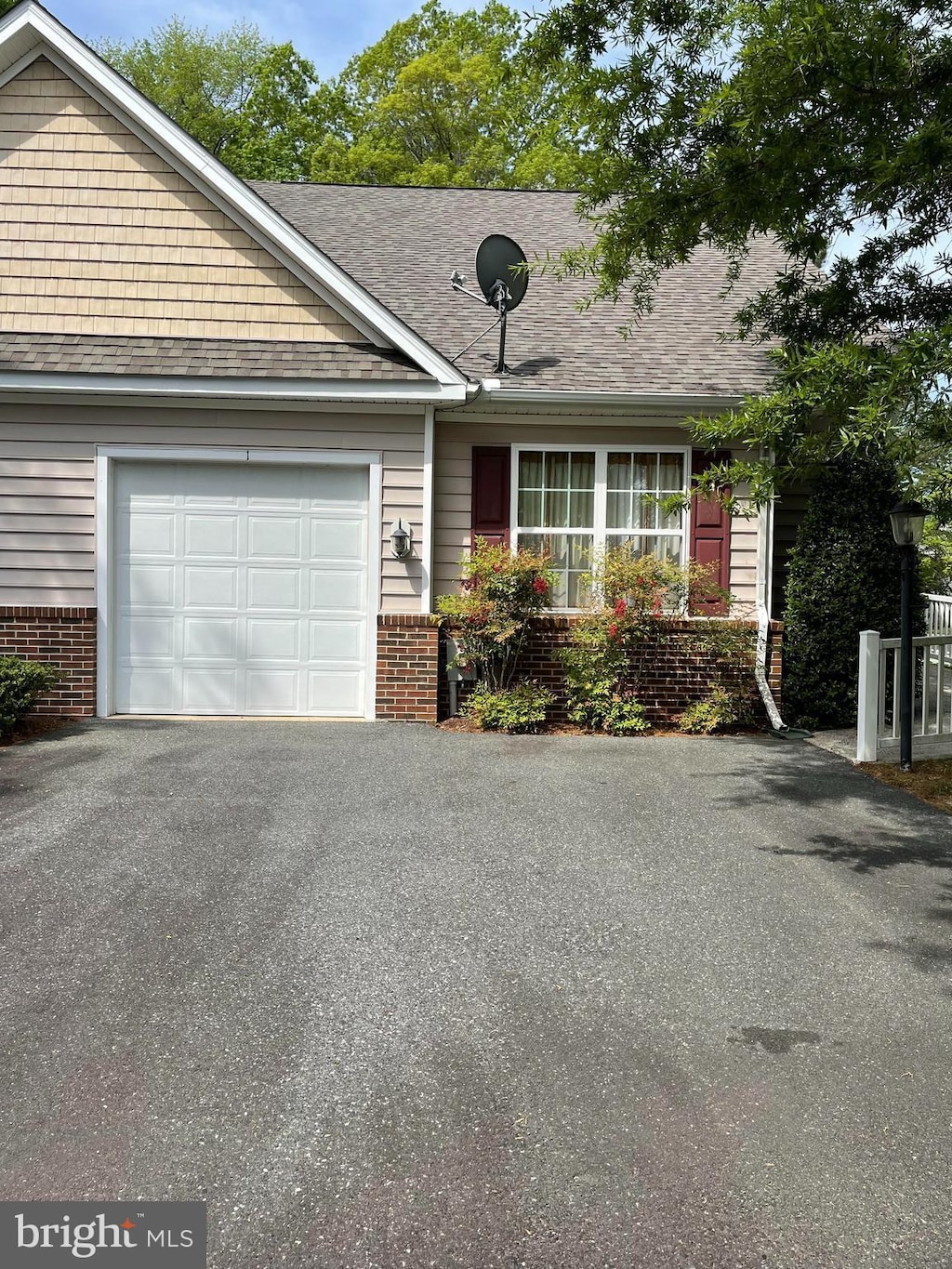 ranch-style home featuring an attached garage, a shingled roof, aphalt driveway, and brick siding