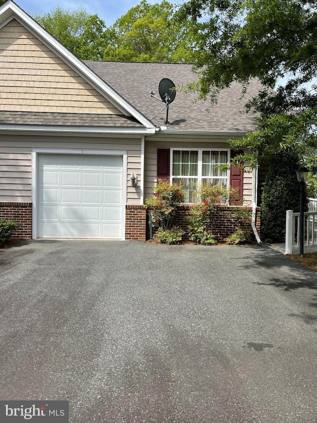 ranch-style home featuring an attached garage, a shingled roof, aphalt driveway, and brick siding