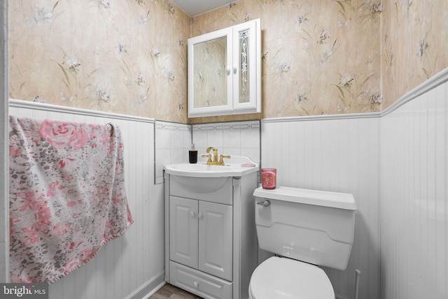 half bath with vanity, wainscoting, and toilet
