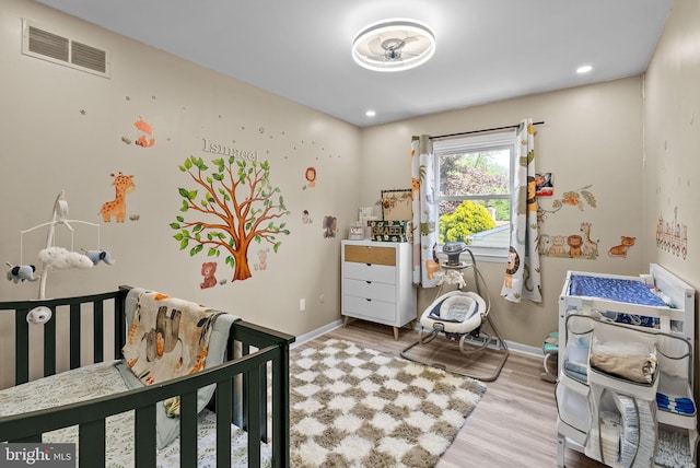 bedroom with baseboards, a nursery area, wood finished floors, and visible vents
