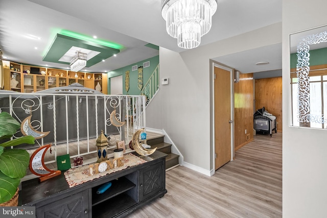 staircase with visible vents, a wood stove, wood finished floors, baseboards, and a notable chandelier