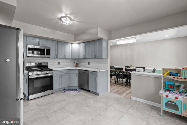 kitchen with appliances with stainless steel finishes, a sink, light countertops, gray cabinets, and backsplash