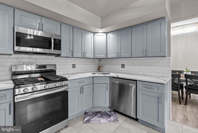 kitchen with a sink, appliances with stainless steel finishes, gray cabinets, and light stone countertops