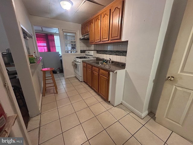 421 52nd St, Baltimore, MD 21224 - kitchen with white gas range, under cabinet range hood, light tile patterned floors, dark countertops, and brown cabinetry