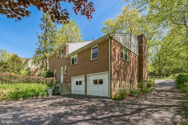 view of property exterior with brick siding, a garage, and aphalt driveway