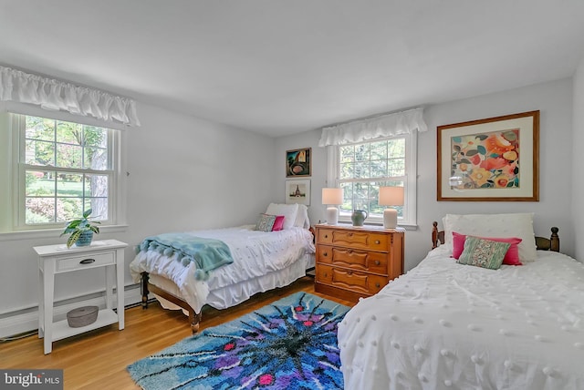 bedroom featuring a baseboard radiator, multiple windows, and wood finished floors